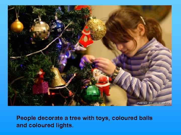 People decorate a tree with toys, coloured balls and coloured lights. 