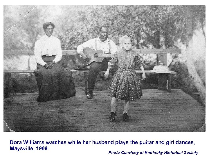 Dora Williams watches while her husband plays the guitar and girl dances, Maysville, 1909.