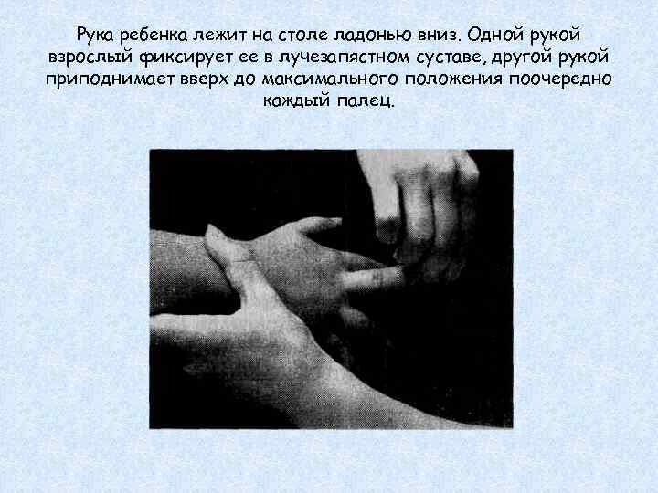 Рука ребенка лежит на столе ладонью вниз. Одной рукой взрослый фиксирует ее в лучезапястном