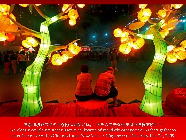 在新加坡春节除夕之夜除旧迎新之际, 一对华人老夫妇坐在象征福橘的彩灯下 An elderly couple sits under lantern sculptures of mandarin orange trees as
