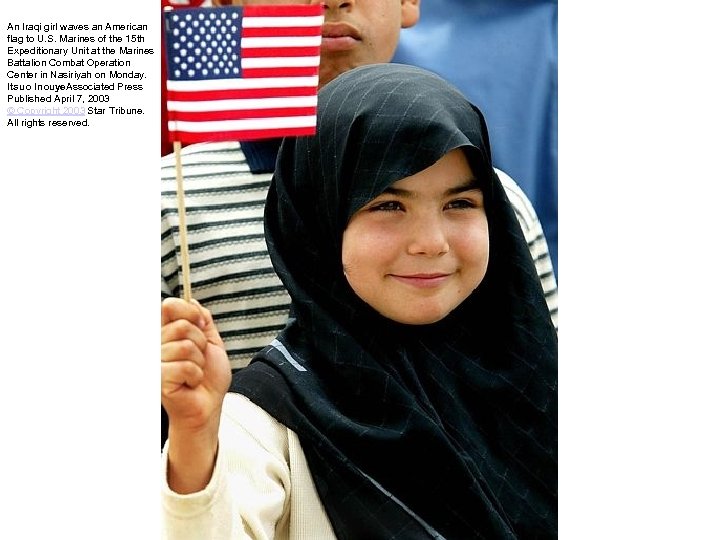 An Iraqi girl waves an American flag to U. S. Marines of the 15