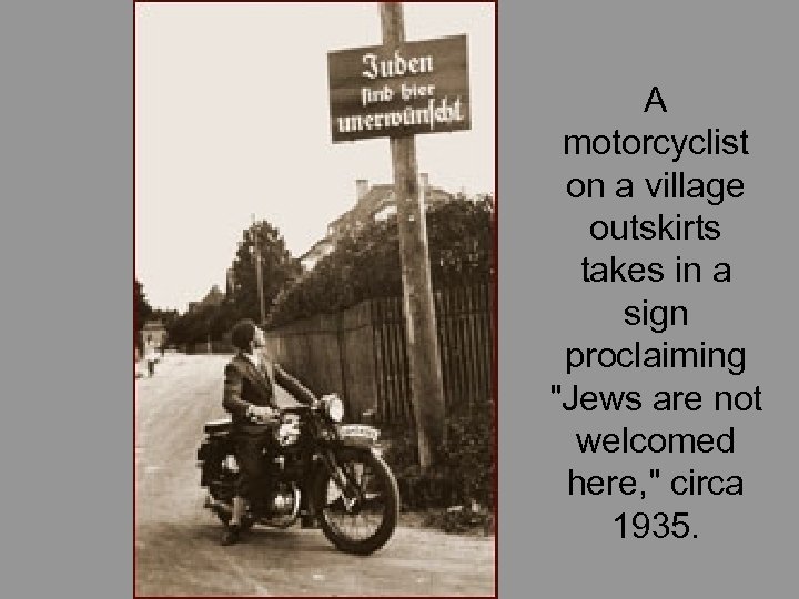 A motorcyclist on a village outskirts takes in a sign proclaiming 