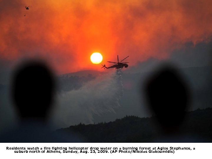 Residents watch a fire fighting helicopter drop water on a burning forest at Agios